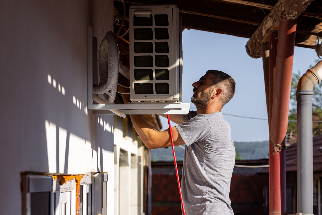 HVAC technician installing an air conditioning unit on an exterior wall during a home AC installation