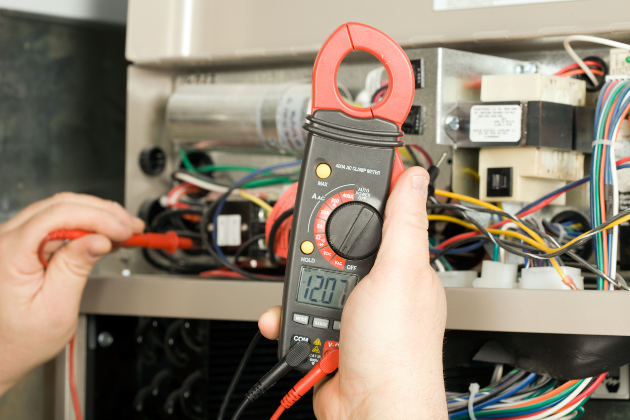  HVAC technician using a clamp meter to test electrical components during furnace maintenance in Alexandria, VA.